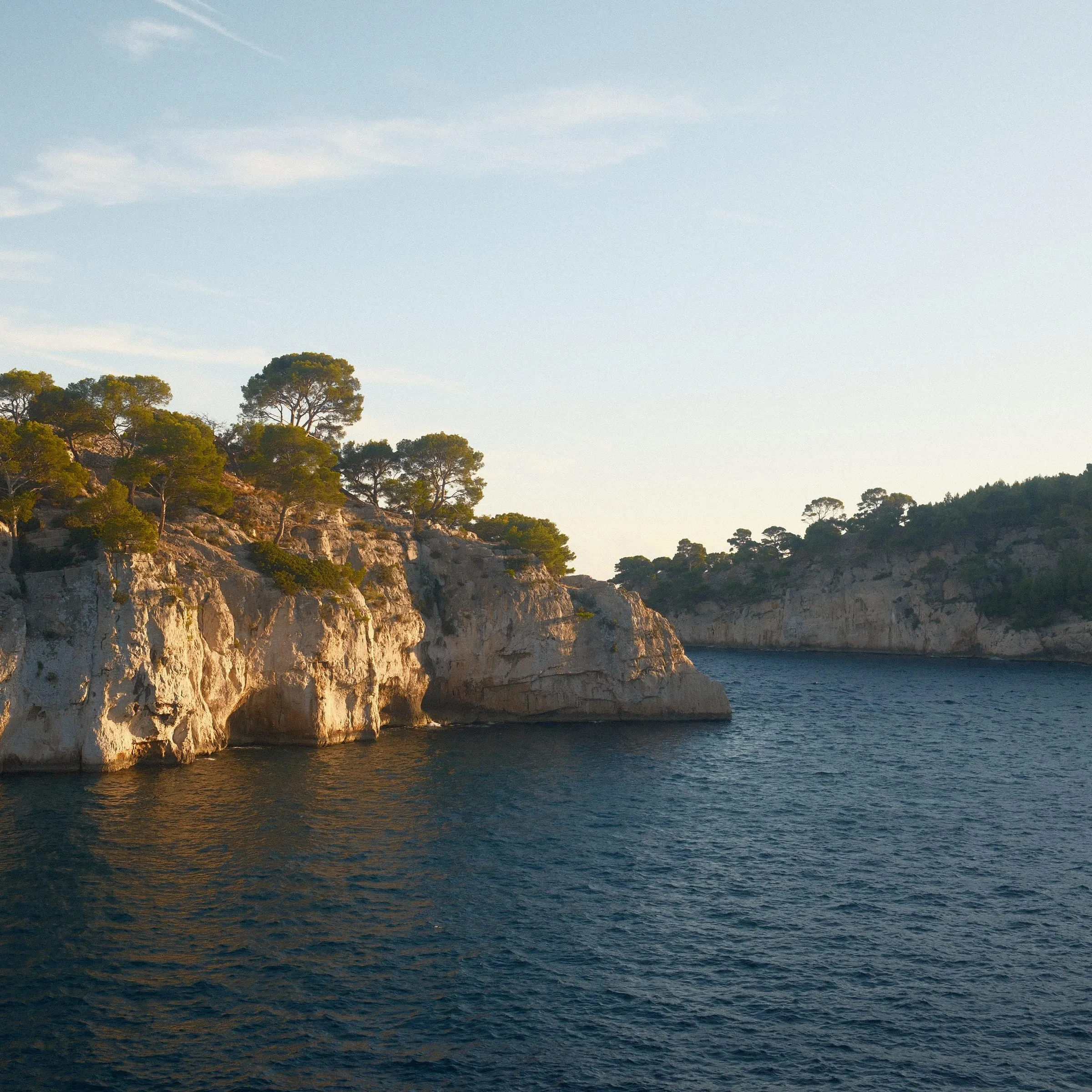 Pine-topped limestone cliffs catch low sun above a dark blue inlet.