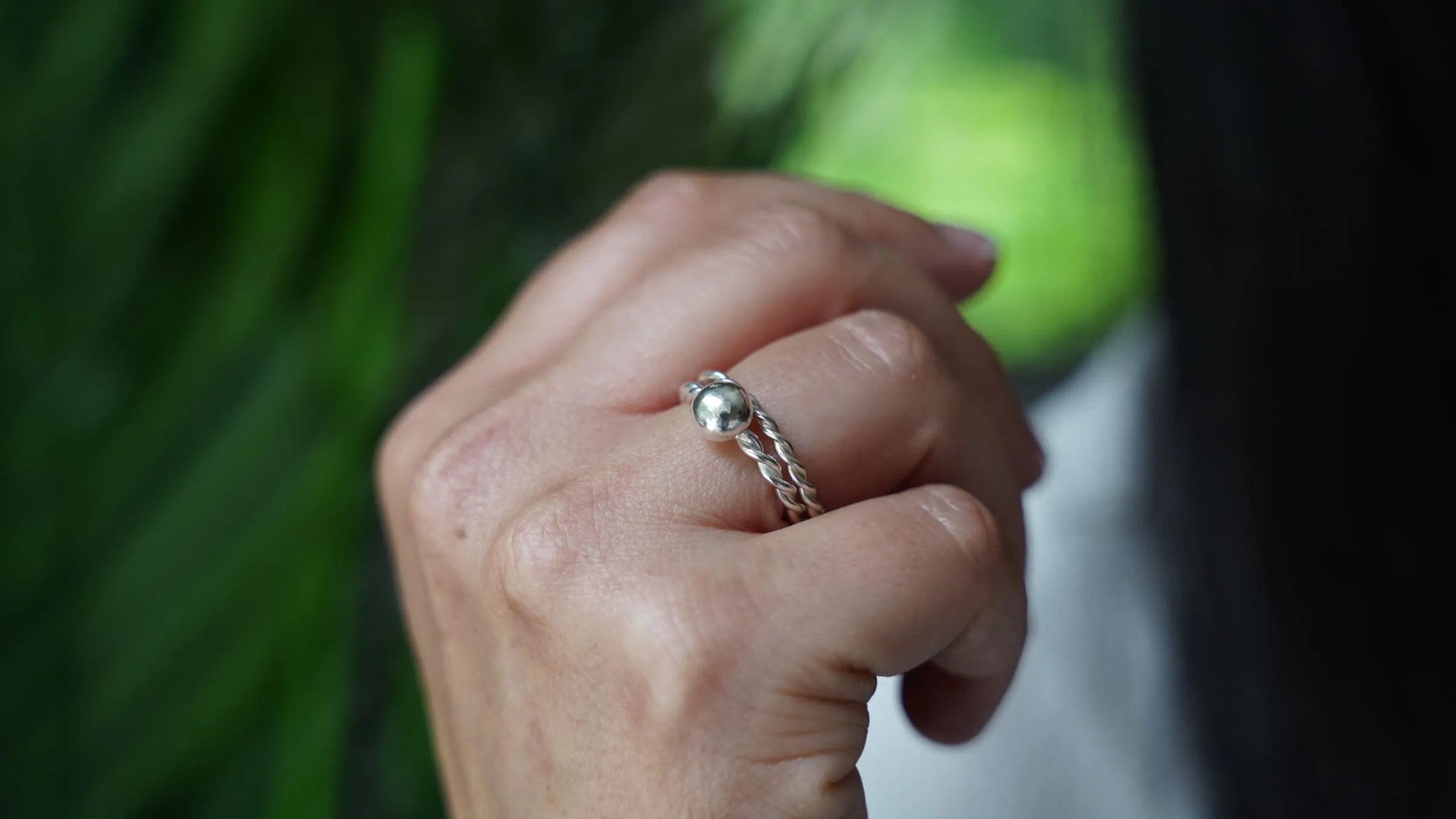 A silver ring on a closed hand against green leaves.