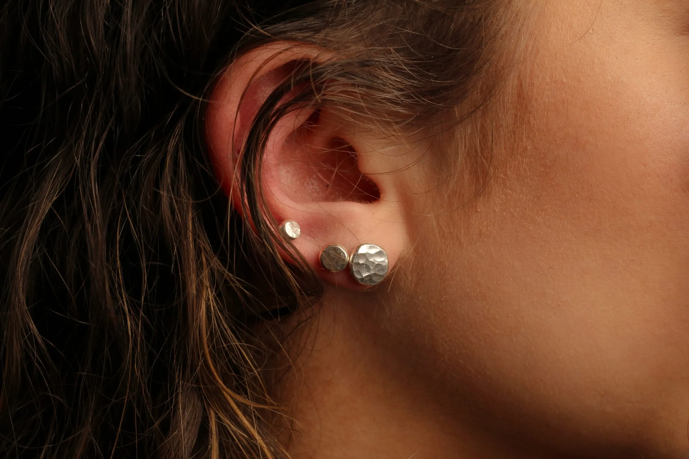 Hammered silver studs in an ear, hair pulled back.