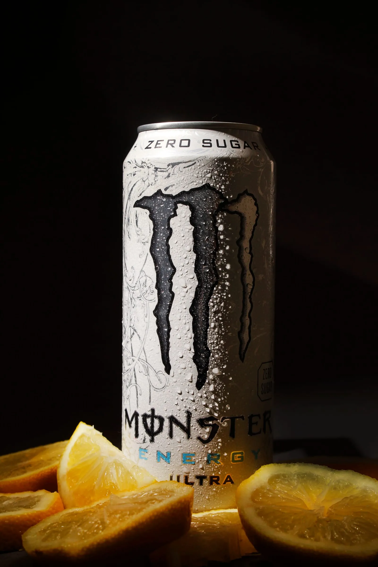 A frosted can of Monster Energy Ultra among orange slices, lit on black.