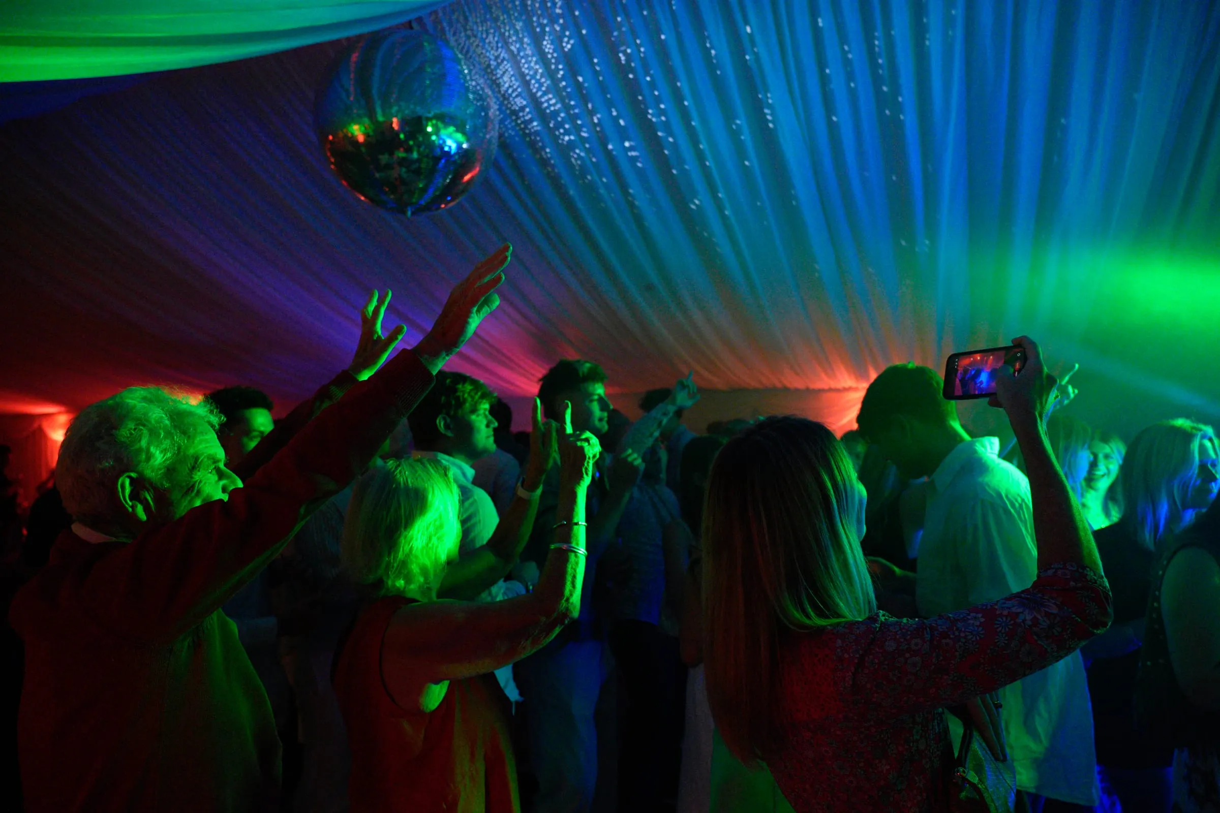 The dance floor under green light and a mirror ball, phones raised.