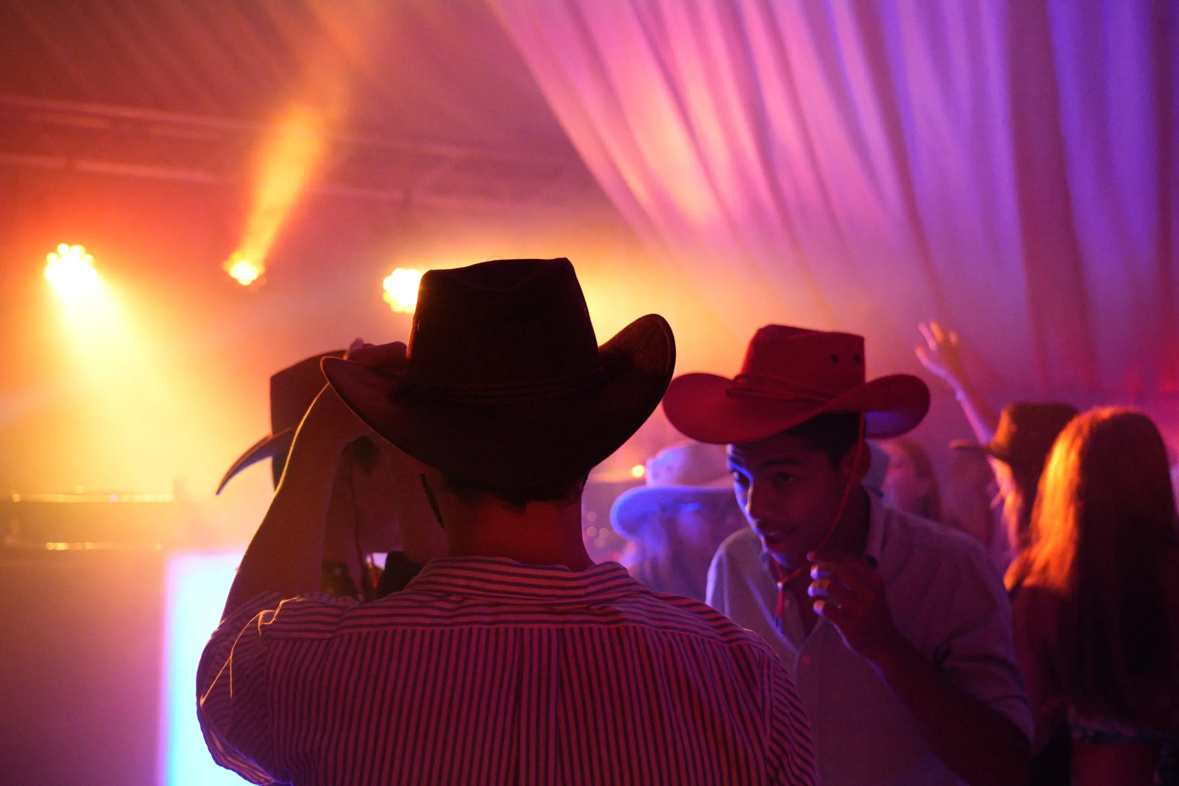 Two guests in cowboy hats, seen from behind, facing the lights.