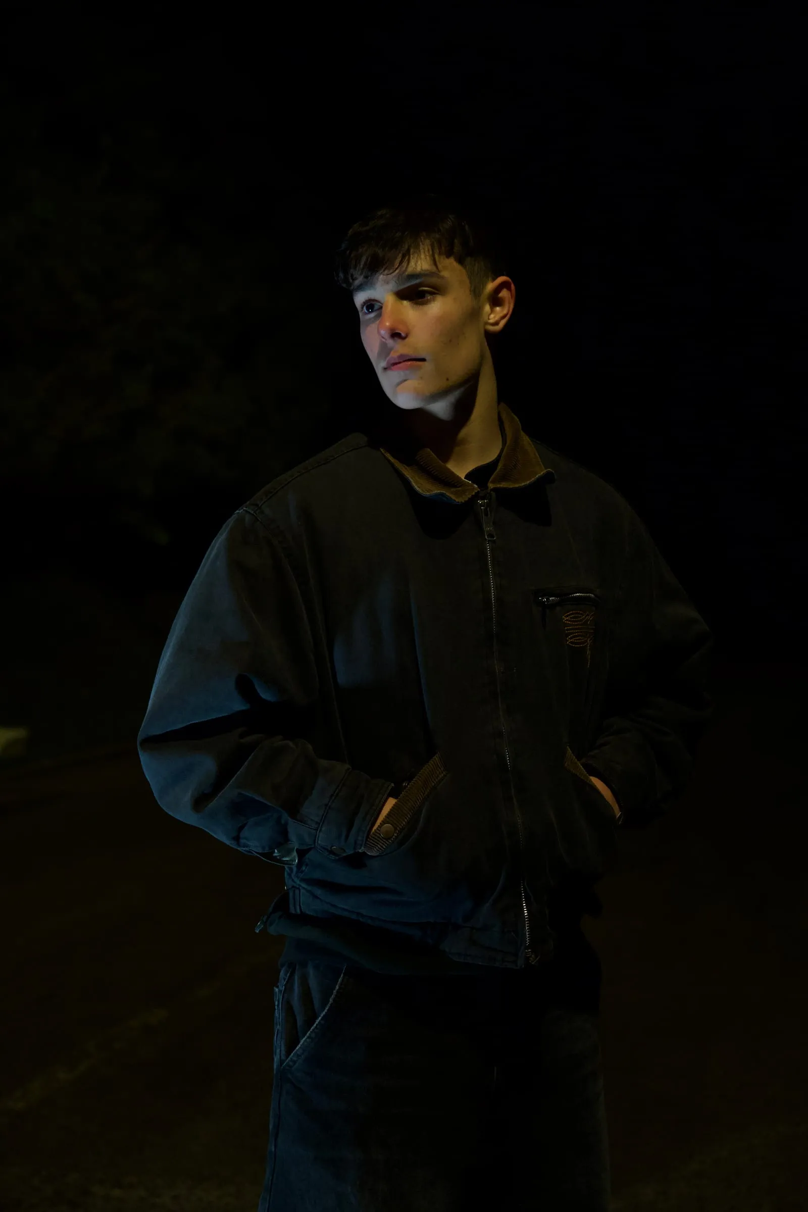 A young man in a dark jacket, lit from one side at night.